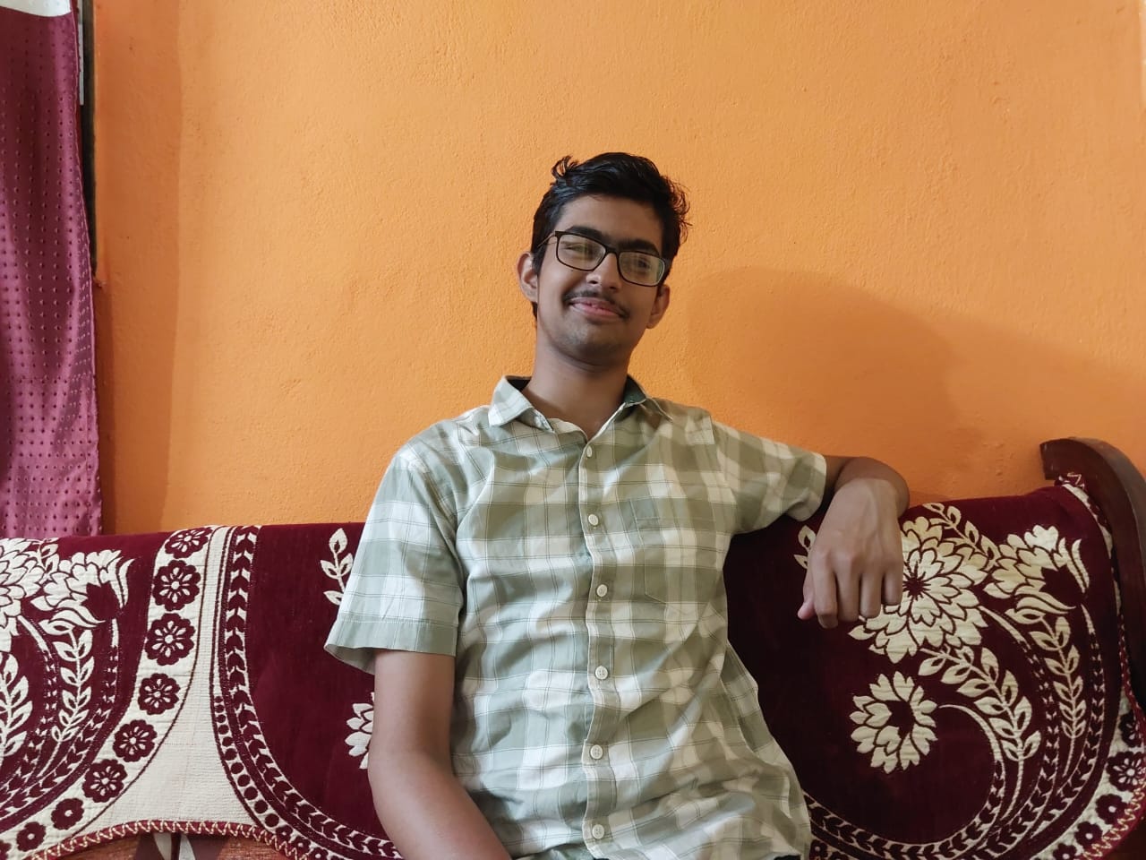 Chaitanya Kulkarni smiling in a red plaid shirt and tortoise shell glasses